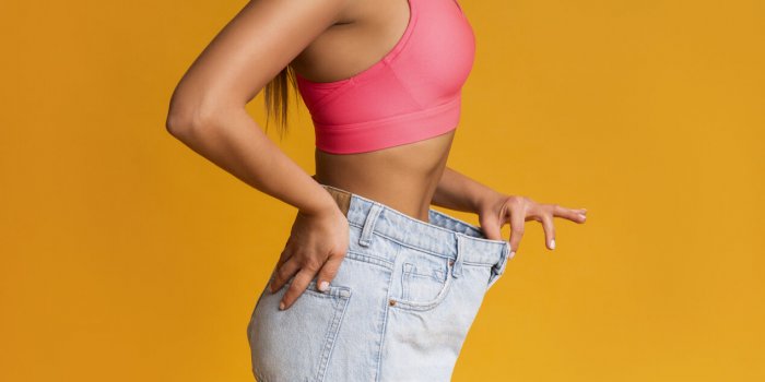 weight loss concept profile portrait of fit girl posing in oversize jeans over yellow background, cropped image with copy...