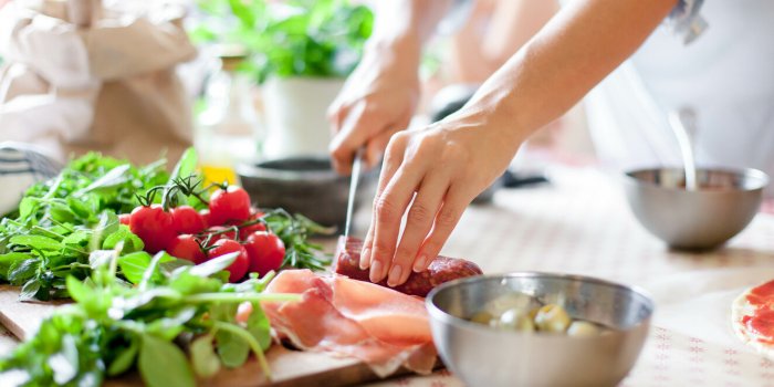 woman is cooking in home kitchen female hands cut salami, vegetables, greens, tomatoes on table on wooden boards ingredie...