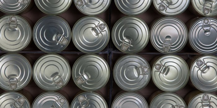 food behind sheet metal lined up tin cans with pull-off lids viewed from above
