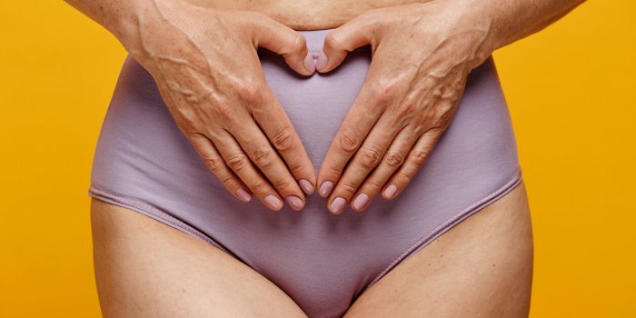 closeup of woman wearing underwear holding hands gently on belly in uterus area