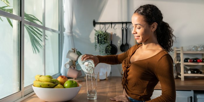 young beautiful latino woman pouring clean water into glass in kitchen attractive active thirsty girl drink or take a sip...