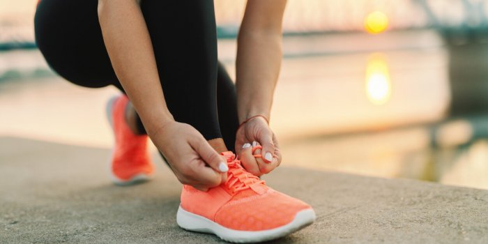 close up of sporty woman tying shoelace while kneeling outdoor, in background bridge fitness outdoors concept
