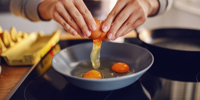 close up of caucasian woman breaking egg and making sunny side up eggs domestic kitchen interior breakfast preparation