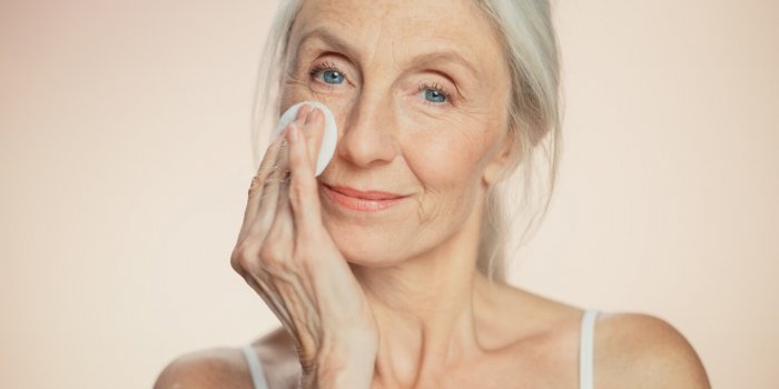 medium potrait beautiful senior woman uses cotton wool pad to clean her perfect face of cosmetics smiling elderly lady w...