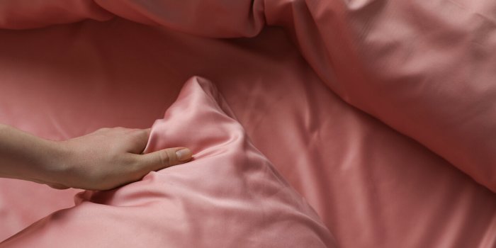 woman making bed with beautiful pink silk linens, closeup view