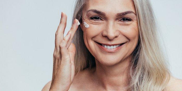 smiling mid adult caucasian woman applying anti aging cream on her face senior female woman applying moisturizer on her f...