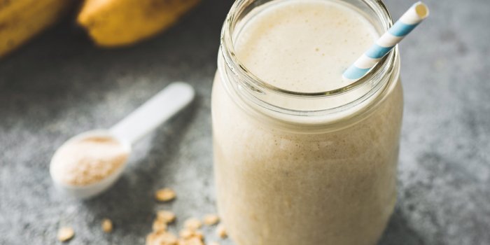 protein milkshake with oats, banana in jar with paper drinking straw on concrete background closeup view, selective focus...