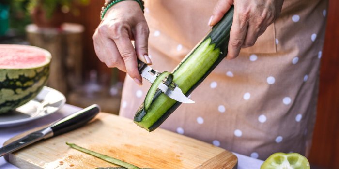woman peeling cucumber making fresh vegetable salad outdoors preparing raw food