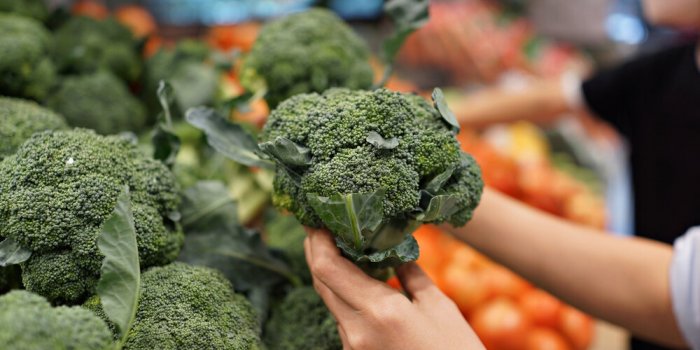 woman's hand choosing fresh broccoli in supermarket concept of healthy vegetarian food