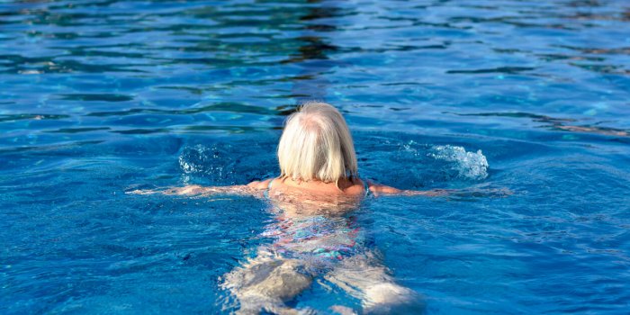 active senior woman swimming in a pool moving away from the camera doing breaststroke in a health and fitness and retirem...