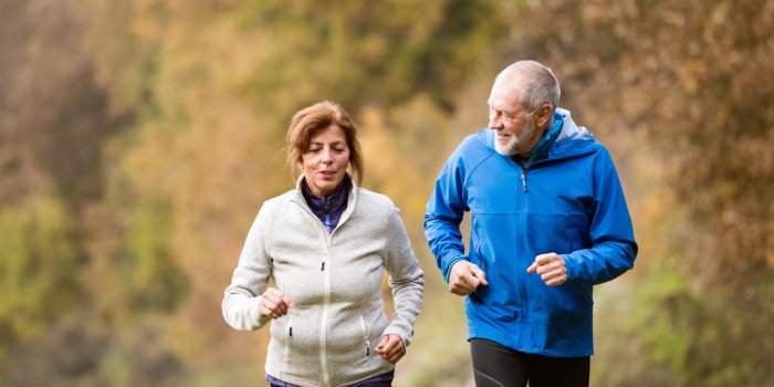 beautiful active senior couple running together outside in sunny autumn forest