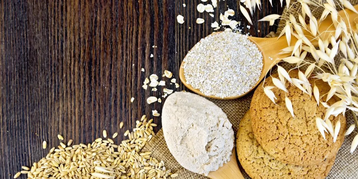 farine et son de foin dans une cuillère, tiges d'avoine, gruau et biscuits sur un fond de sac sur une planche de bois