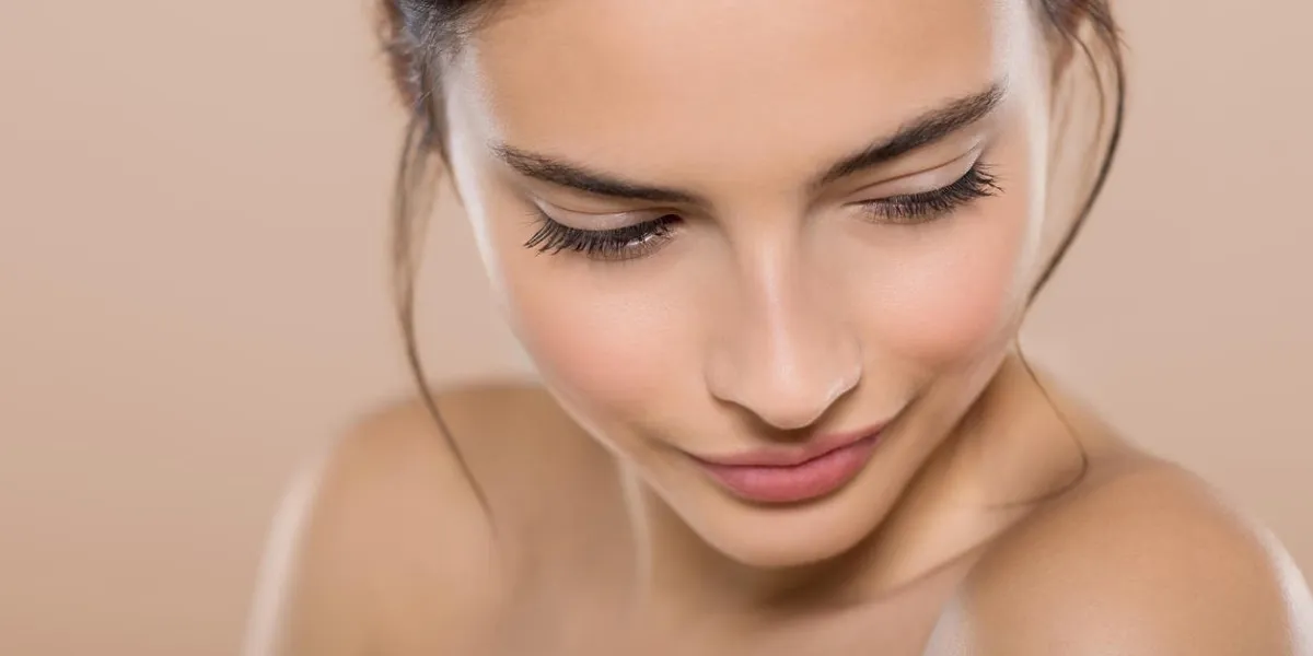 beauty portrait of young woman looking down isolated on background closeup face of a beautiful young brunette woman with perfect healthy skin looking down and smiling beauty and spa treatment
