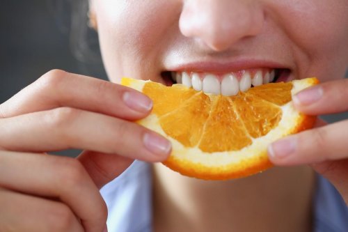 beautiful brunette smiling woman eat sliced raw tasty orange half at kitchen in the morning closeup weight loss beauty fi...