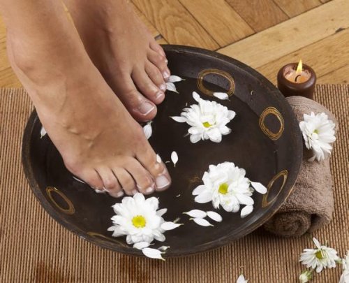 pieds féminins dans le pied spa avec des fleurs, une serviette et une bougie