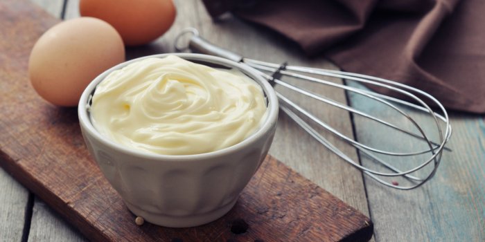 homemade mayonnaise in bowl with eggs and spice on wooden background