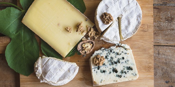 various french cheeses, nuts, fig leaf on the wooden cutting board old wooden background, top view