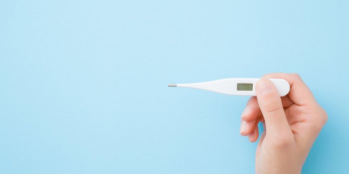 young woman hands holding white digital thermometer on pastel blue background fever and healthcare concept closeup point ...