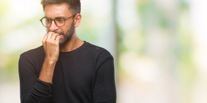 adult hispanic man wearing glasses over isolated background looking stressed and nervous with hands on mouth biting nails...