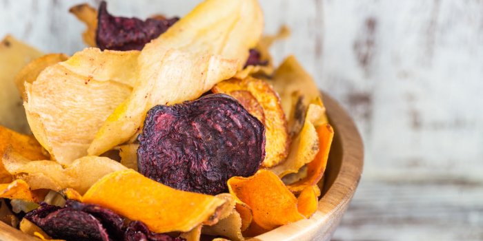 bowl of healthy snack from vegetable chips, such as sweet potato, beetroot, carrot, parsnip on light wooden background