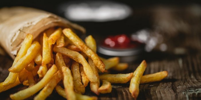 french fries in a basket with ketchup and salt on a dark background