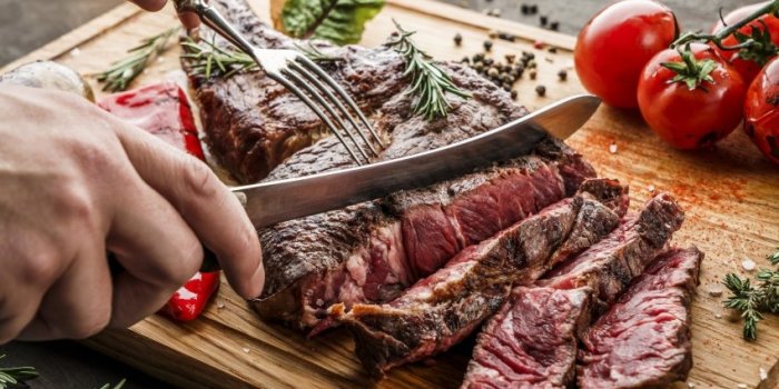hands cut grilled tomahawk meat medium rare or rib eye steak on wooden cutting board with grilled vegetables on dark back...