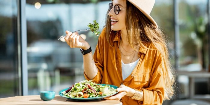 stylish young woman eating healthy salad on a restaurant terrace, feeling happy on a summer day