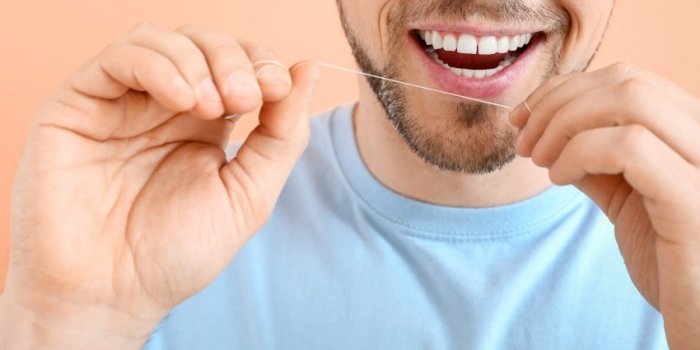man flossing teeth on color background, closeup