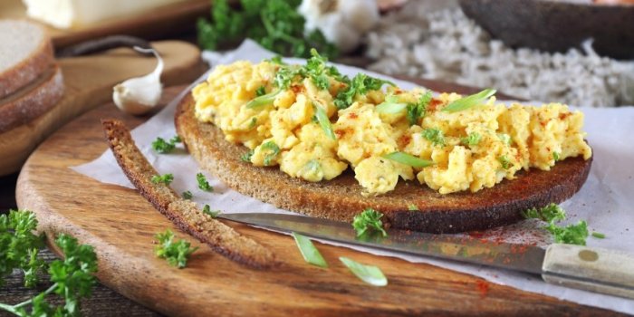 scrambled eggs on slice of fried rye bread, parsley and green onion dressing on wooden cutting board