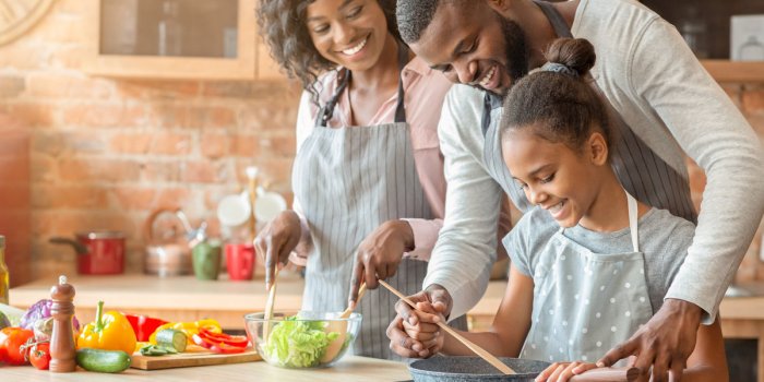 kind afro parents teaching their adorable daughter how to cook healthy food in kitchen, copy space