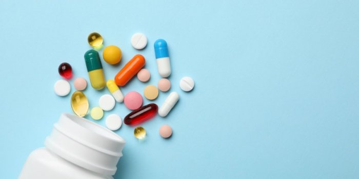 bottle and scattered pills on color background, top view space for text