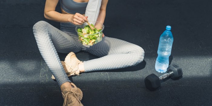 being healthy involves a diet unrecognizable caucasian young woman in gray sportswear sitting on the dark floor next to a...