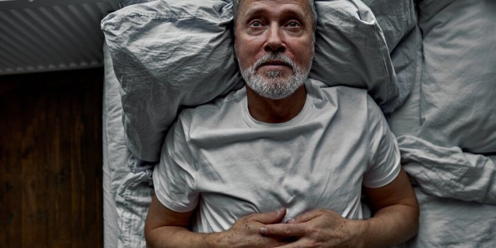 middle-aged man lying down in bed on pillow, having insomnia sleeping disorder alone at home