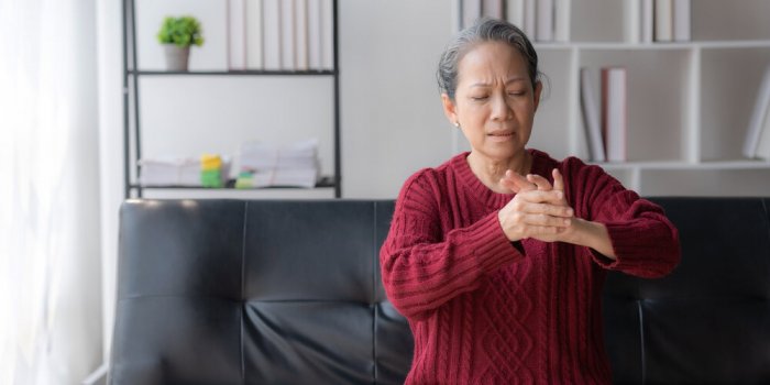 asian old woman with body aches, leg pain, bone pain, stiff muscles, arm pain, hand pain, sitting on the sofa in the livi...
