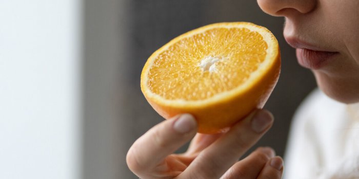 sick woman trying to sense smell of half fresh orange, has symp