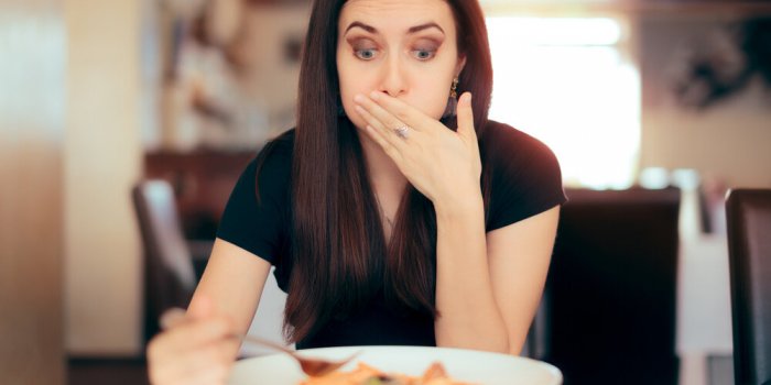 woman feeling sick while eating bad food in a restaurant