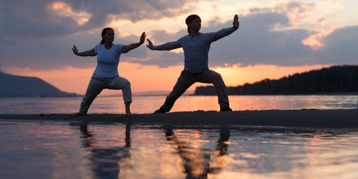 man and woman doing tai chi chuan at sunset on the beach solo