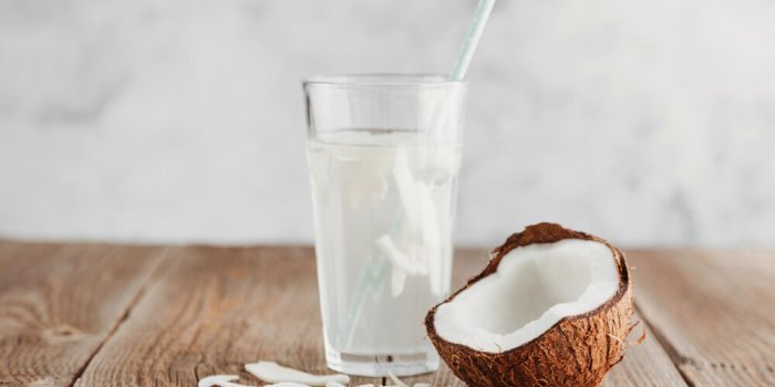 a glass of fresh organic coconut water, milk on a wooden table and a ripe half of a coconut nearby refreshing vegetarian ...