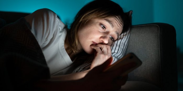 young anxious woman lying in bed staring at smartphone screen at night, reading about depression symptoms in internet, ph...
