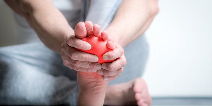 causian man holds hands to his painful feet, pain in foot, red color is area of pain