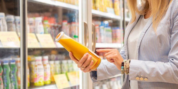woman reading ingredients information on orange juice bottle's etiquette