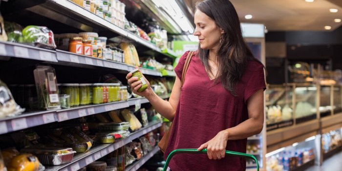 young woman shopping in grocery store mature woman checking food label in supermarket latin woman holding shopping basket...