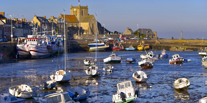 port at low tide at the end of the sunny day and church of saint-nicolas of barfleur, a commune in the peninsula of coten...