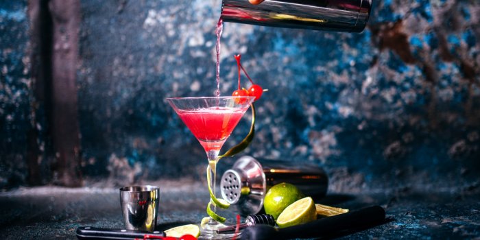 barman preparing and pouring red cocktail in martini glass cosmopolitan cocktail on metal background