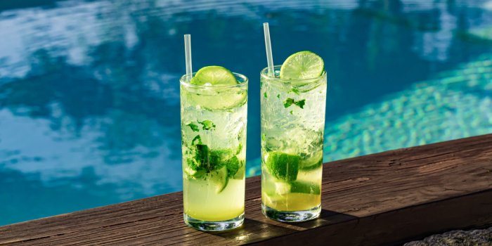 two fresh and cold mojitos with ice cubes, lime slices and mint leaves on a turquoise pool background