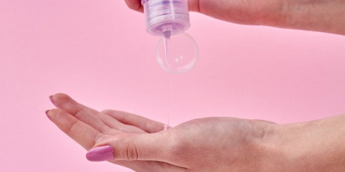 woman's squeezing shampoo on her palm close up transparent liquid soap flow from a bottle isolated on pink background