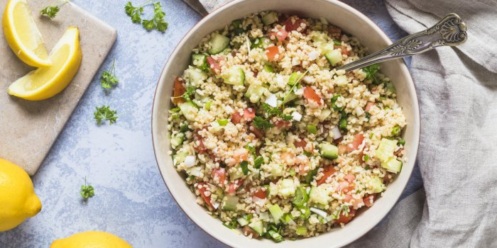 a large bowl of fresh organic healthy tabouli tabboleh salad with bulgur, tomato, cucumber, lemon and parsley there are s...