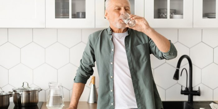 healthy senior man drinking glass of water in his kitchen, elderly gentleman showcasing the importance of hydration for w...