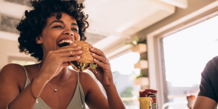 african woman eating stack burger at restaurant with friends happy young woman having junk food at cafe with friends