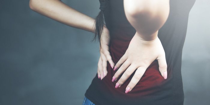 young woman with backache lower back pain colored in red isolated on dark background